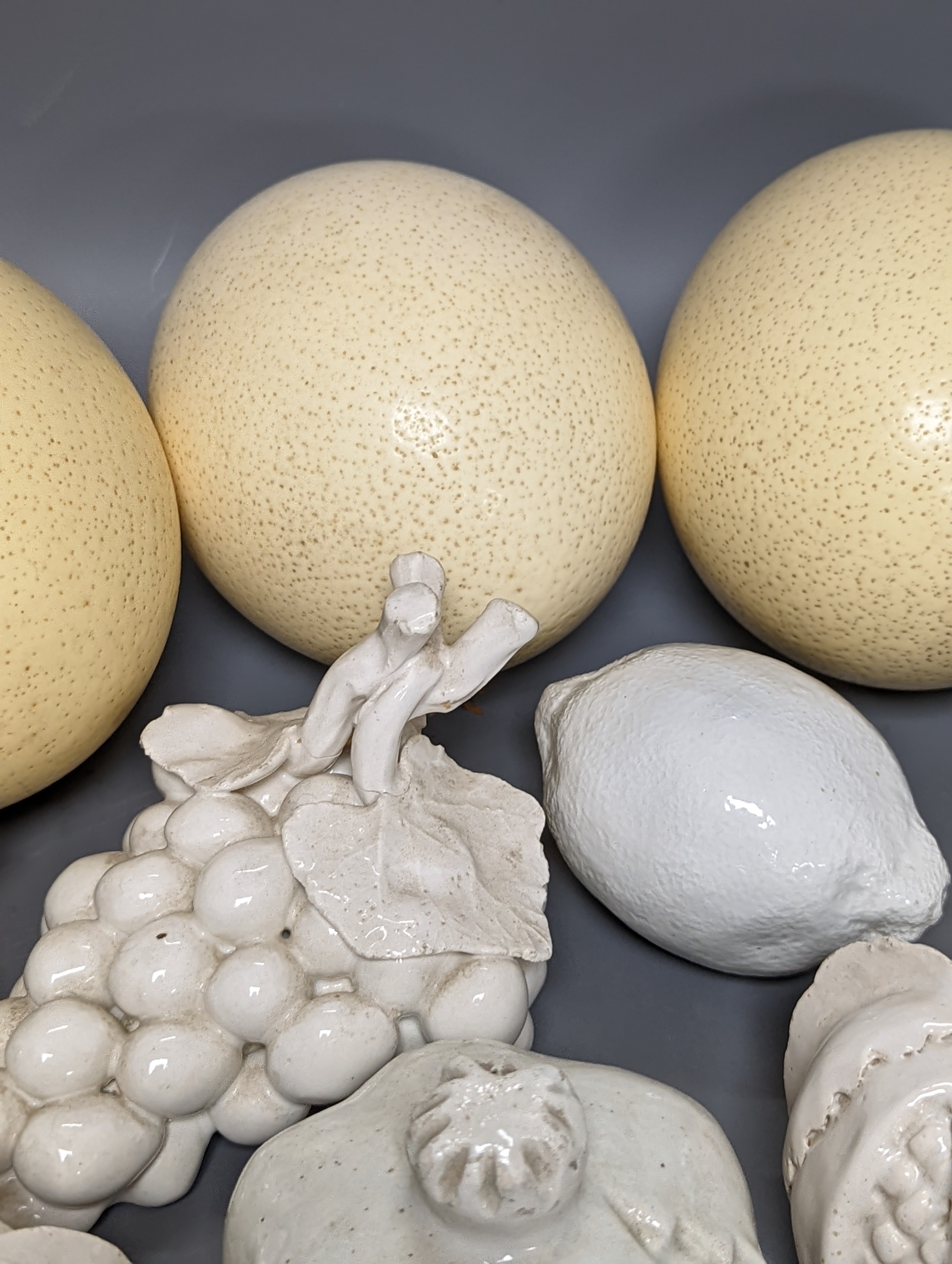 A decorative collection of tin glazed model fruits, together with three ostrich eggs